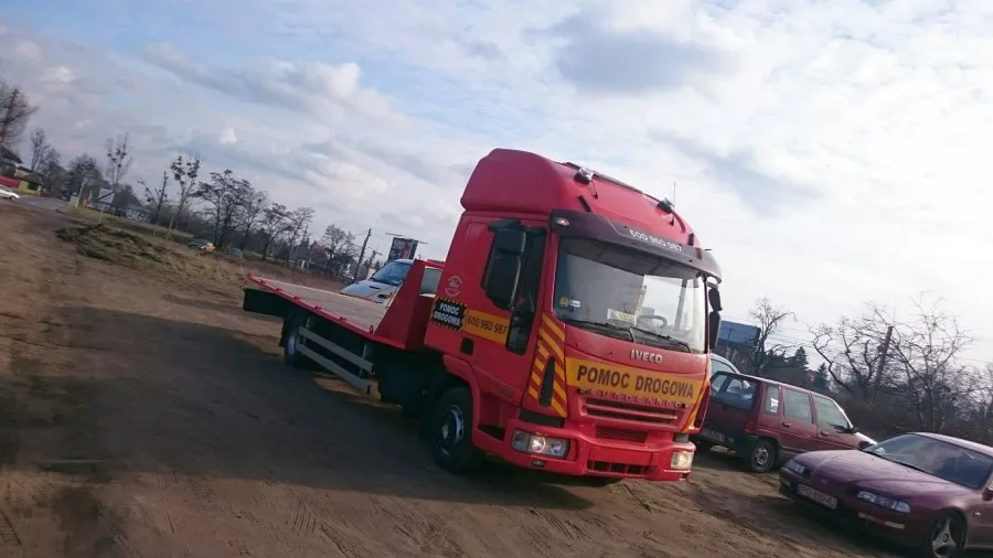 Na brudnym parkingu zaparkowane są czerwone holowniki.
