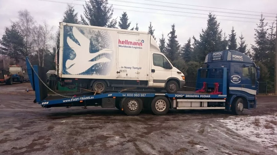 Biała furgonetka podłączona do ciężarówki z platformą.