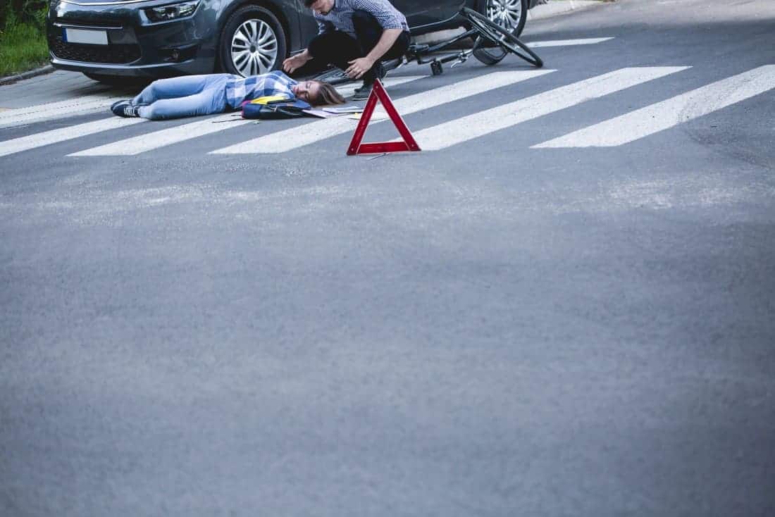 Mężczyzna leżący na ziemi przed samochodem.
